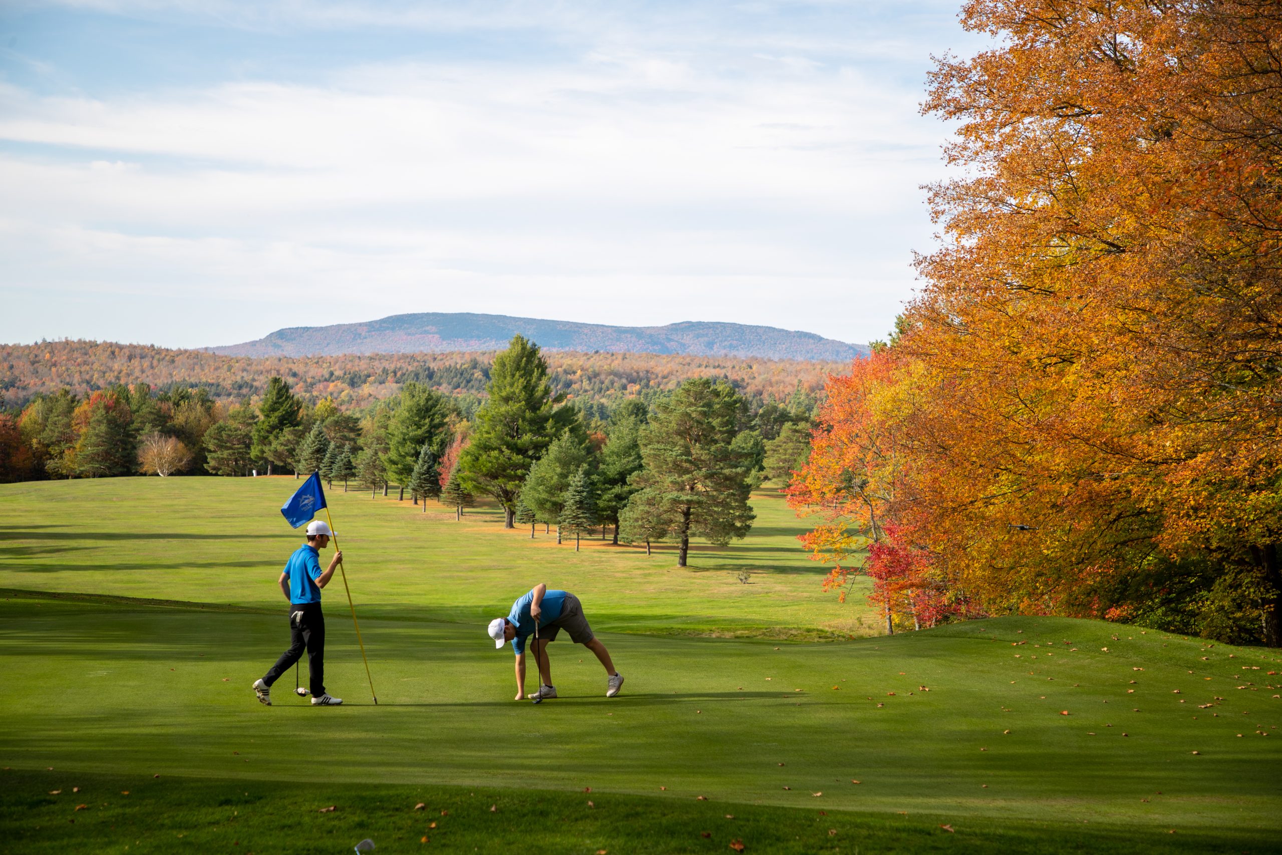 Golfers on 15 green with fall foliage and mountain backdrop